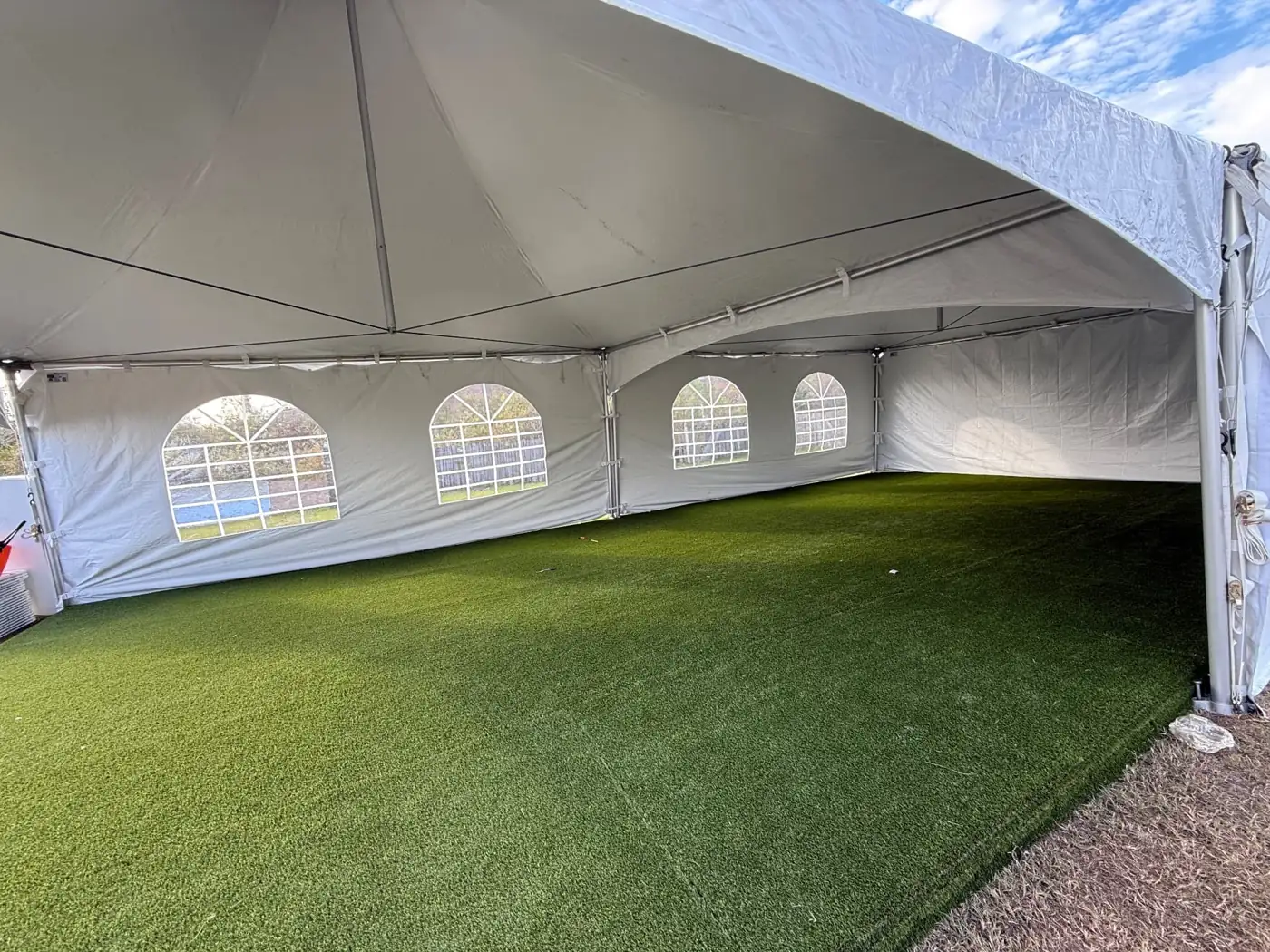 Interior of a white event tent with windowed sidewalls and grass floor